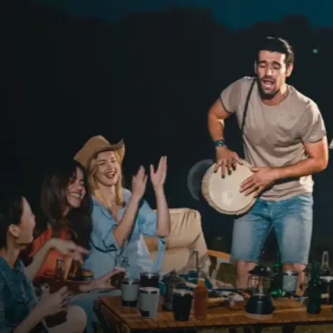 Group of friends enjoying a night outdoors in Egypt, with one person playing a drum and others clapping and smiling