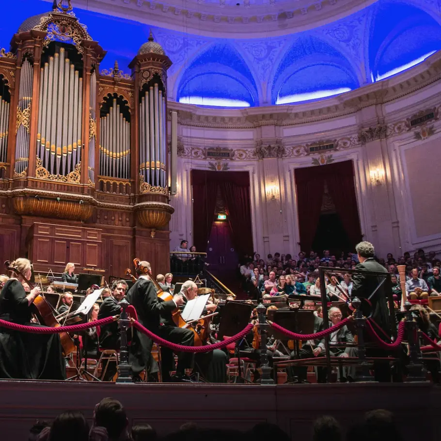 Orchestra performing in a grand concert hall in Italy with a large pipe organ and audience in the background.