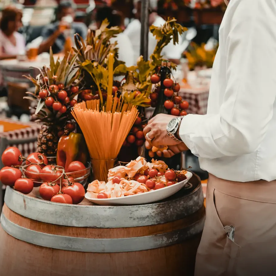 Close-up of a person preparing an Italian food display with tomatoes, pasta, and grapes.