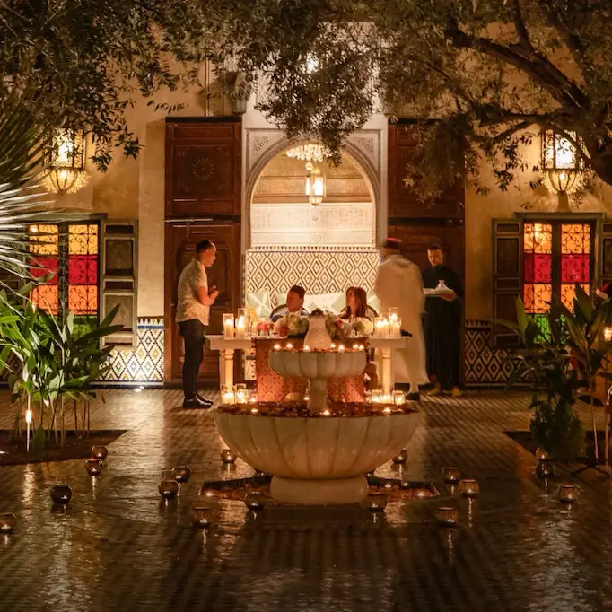 Candlelit dinner setting in a Moroccan courtyard with a central fountain.