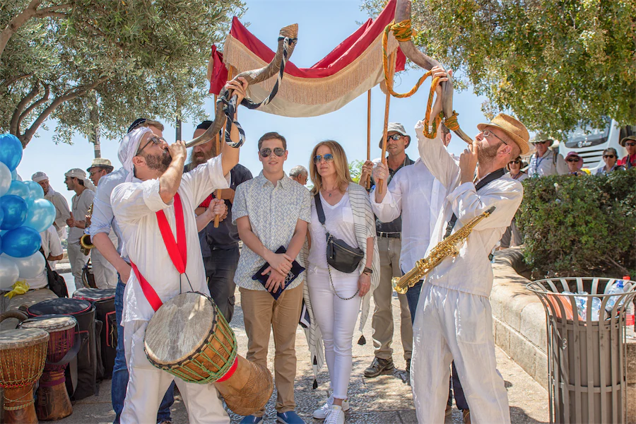 Traditional Jewish musicians blow the shofar and play drums beneath a chuppah during a festive moment.
