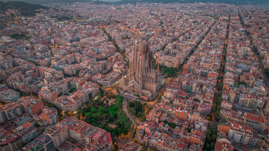 A magnificent aerial shot of Barcelona’s iconic La Sagrada Familia, with its towering spires amidst the surrounding urban landscape, showcasing the city’s mix of historical and modern architecture.