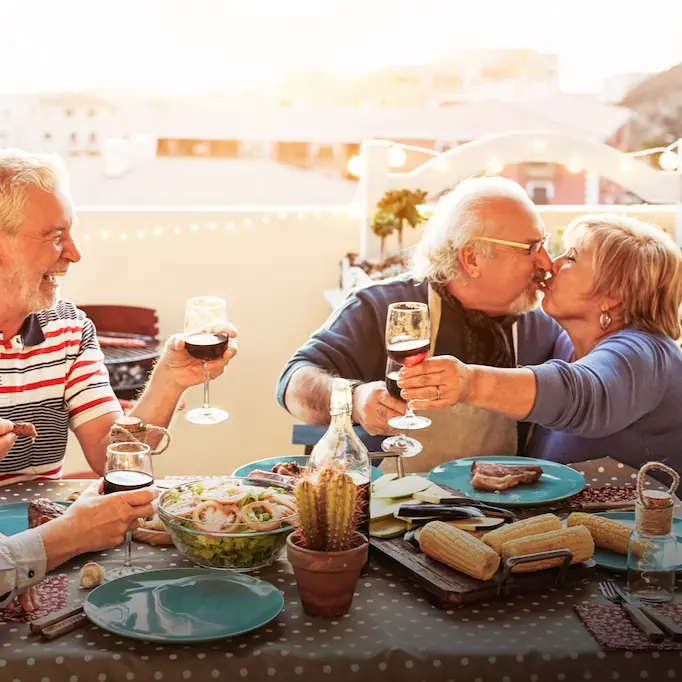 Elderly friends enjoying a festive outdoor dinner with Portuguese food, wine, and grilled corn